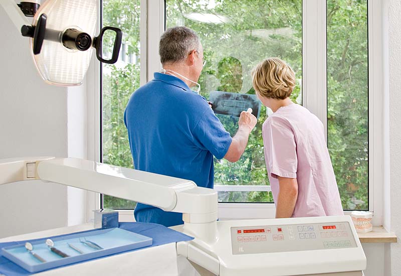 Zahnarzt Ulf Heinze mit Assistentin beim Ansehen eines Röntgenbildes vor einem Fenster.